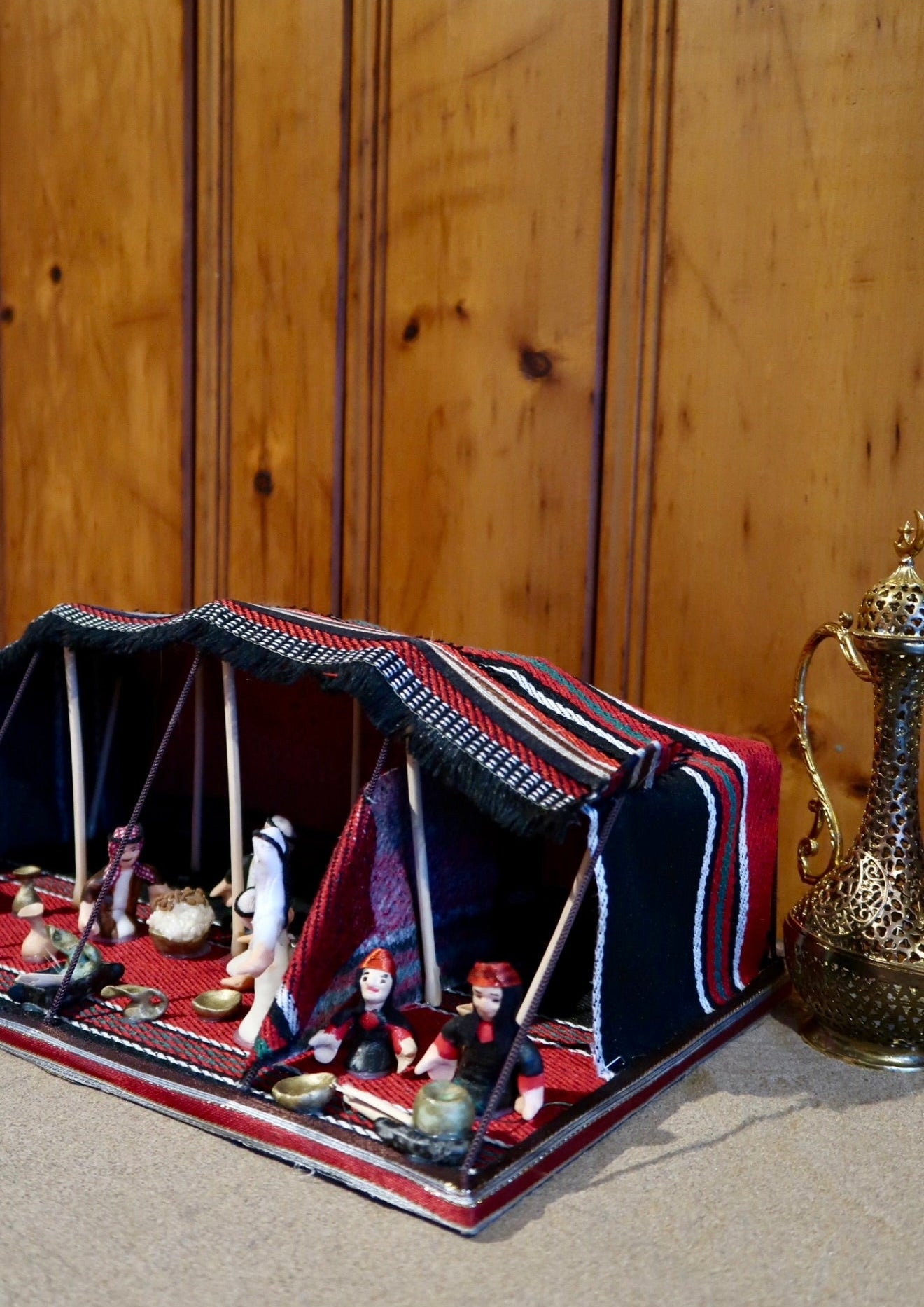 Model of a tent with figurines and a decorative teapot on a wooden surface